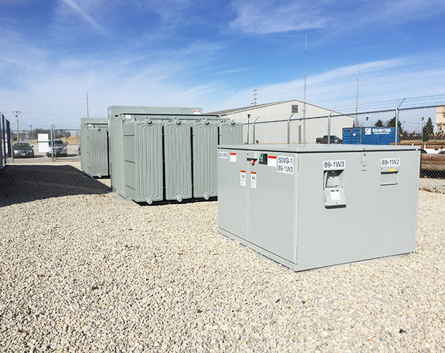 right side profile of an installed gray P M H pad mounted gear for outdoor distribution, 14.4 kV and 25 kV with roof and doors closed and fenced PMH Pad-Mounted Gear